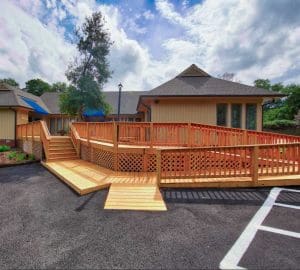 A sprawling wooden porch, skillfully designed and built by Deck Creations, boasts a handicap-accessible ramp for convenience.