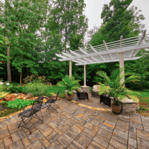 Stunning white pergola gracefully covering a warm and earthly-colored stone hardscape patio, expertly designed by Deck Creations.