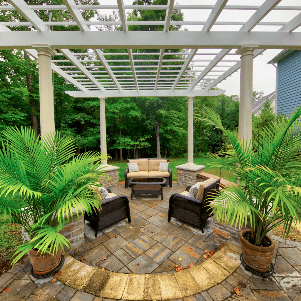 Stunning white pergola gracefully covering a warm and earthly-colored stone hardscape patio, expertly designed by Deck Creations.