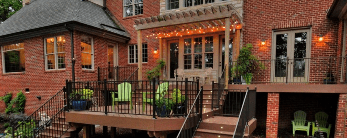 Stunning brick house with a pergola, custom deck and black metal railing by Deck Creations.