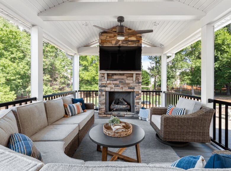 Beautiful outdoor covered patio with stone fireplace, tv, raised wooden ceilings, and black railing.