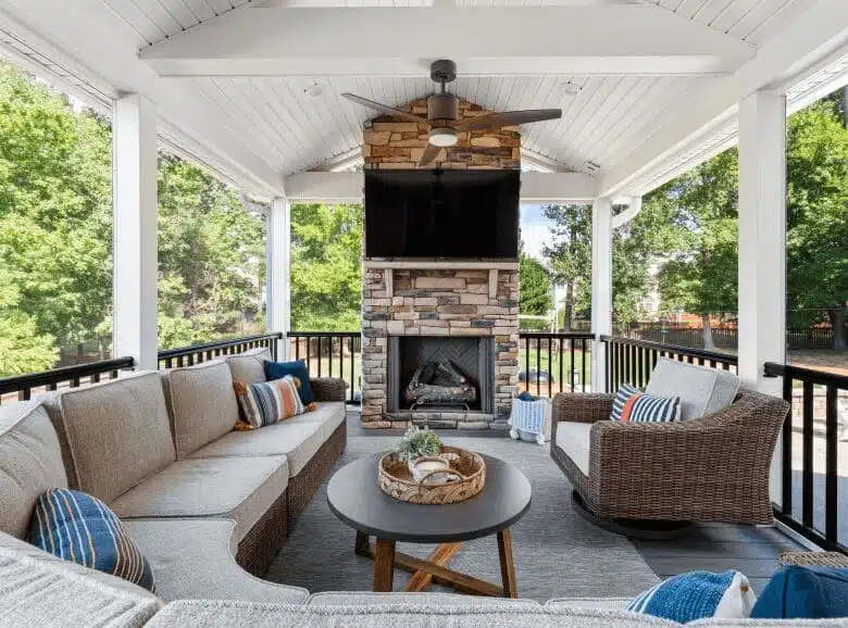 Beautiful outdoor covered patio with stone fireplace, tv, raised wooden ceilings, and black railing.