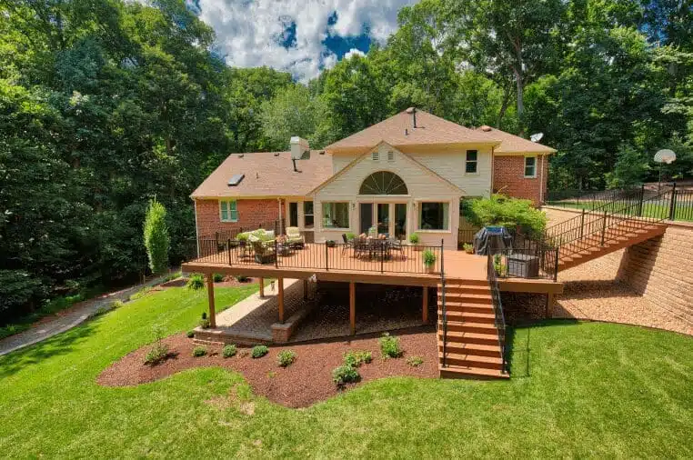 A magnificent wooden deck, expertly designed and built by Deck Creations, graces the side of a stunning house. The light brown wood and black metal railing create an elegant contrast.