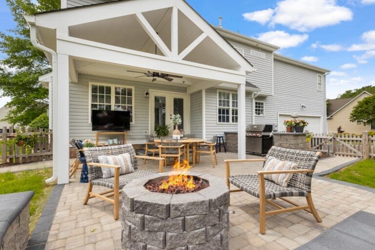 A captivating outdoor space designed by Deck Creations, featuring a covered patio with a white wood ceiling extending into an inviting fire pit area.