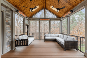 A screened porch features a wooden ceiling, two ceiling fans, and two wicker sofas with white cushions. The serene surroundings and lush trees are visible through the screens, offering the perfect blend of comfort and nature from deck to view.