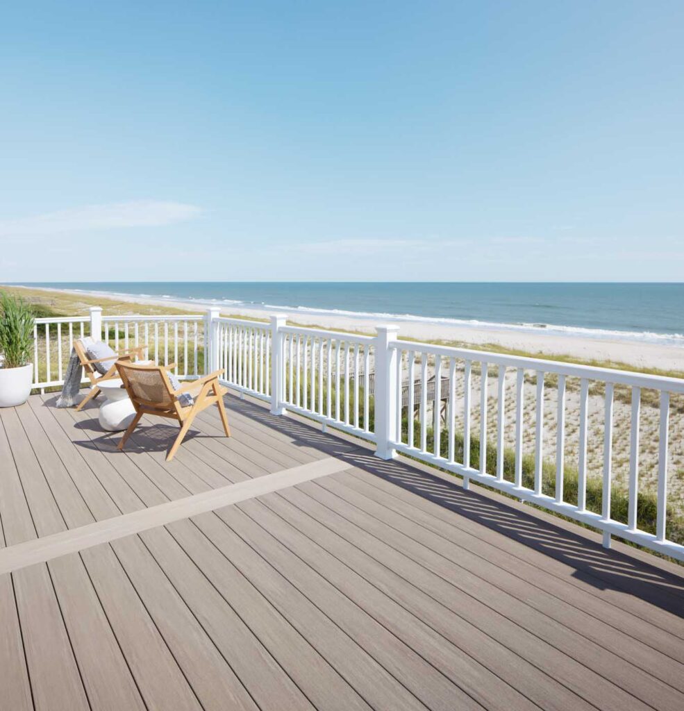 A cozy wooden deck adorned with chairs offers a pristine view of the sandy beach and endless ocean under a clear blue sky.