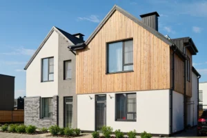 This modern duplex house features a stylish mix of gray brick and stucco siding in one section, while the other boasts elegant wood paneling. Both sections showcase pitched roofs and large windows for a seamless blend of design and function.