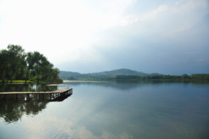 A wooden dock extends over a calm lake, bordered by trees and distant hills under a partly cloudy sky—perfect for outdoor living or inspiring your next exterior renovation.