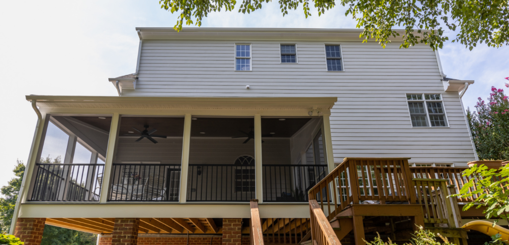 A two-story white house with a screened porch, ceiling fans, and an adjacent wooden deck, viewed from the backyard.