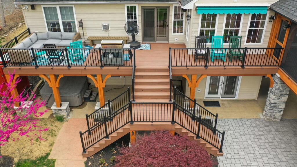 A two-level wooden deck with black railings, outdoor furniture, and stairs leading to a garden with paving stones and landscaping.