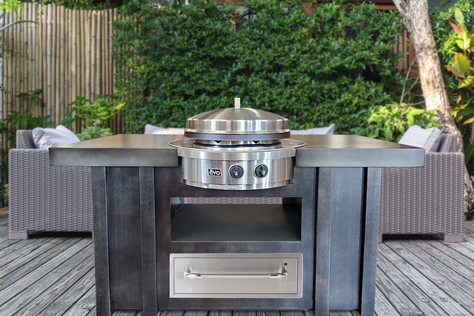 Outdoor island in dark cabinetry with a round stainless flat-top grill, surrounded by patio seating — available from Deck Creations.