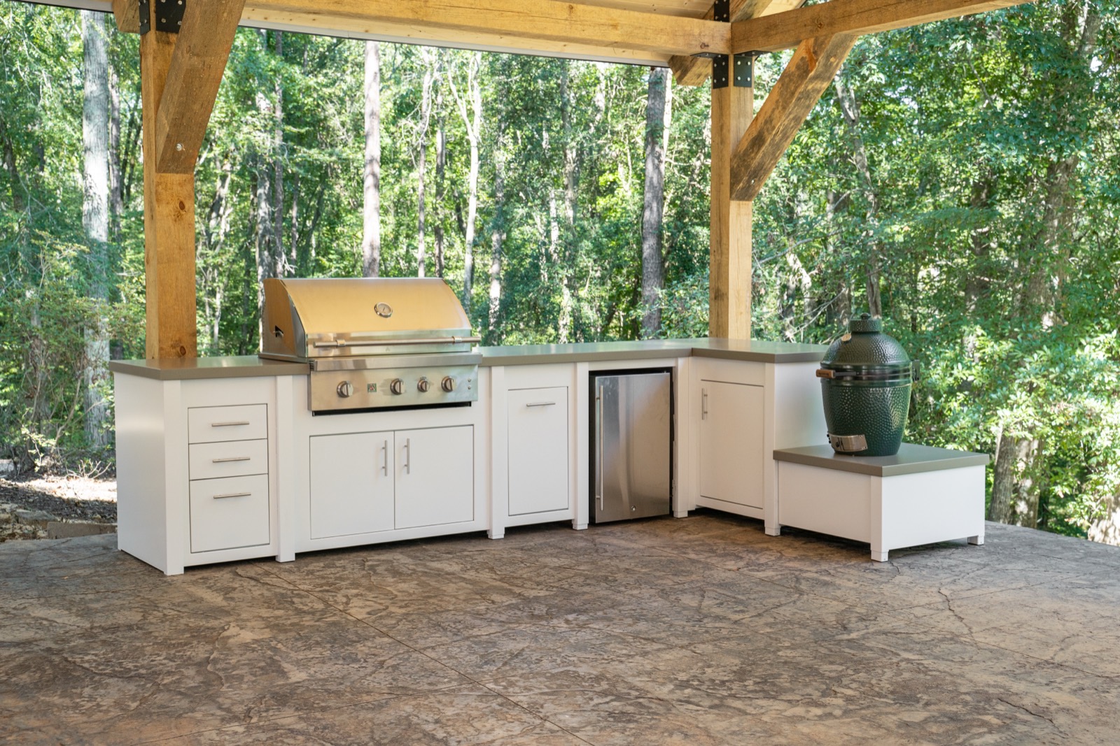 White outdoor kitchen with a grill and ceramic grill built into a timber pavilion, from the custom cabinetry line Deck Creations sells.