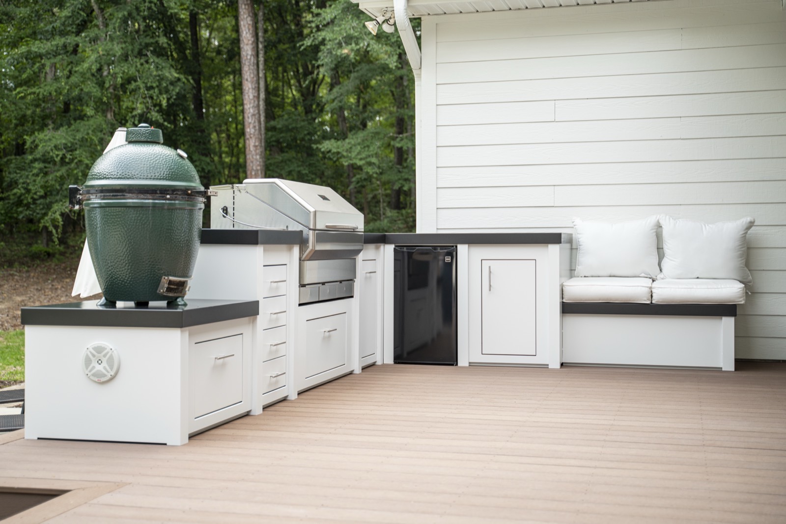 White L-shaped outdoor kitchen with built-in bench seating on a composite deck — cabinetry sold by Deck Creations.