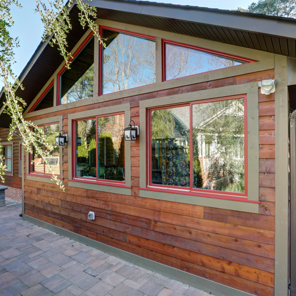 Rustic cabin-style sunroom with stained wood siding, adorned with red trim around glass windows.